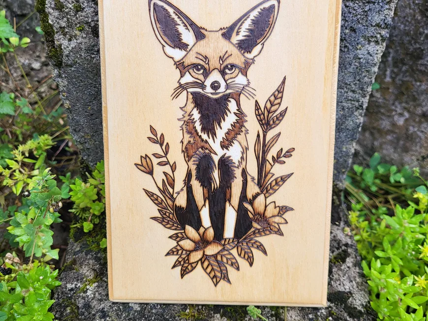 A wood-burned fennec fox among leaves on a wooden plaque