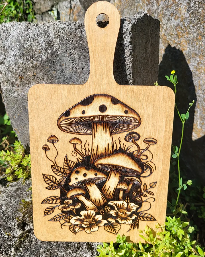 A wood-burned mushroom cluster on a wooden board, propped against a mossy rock